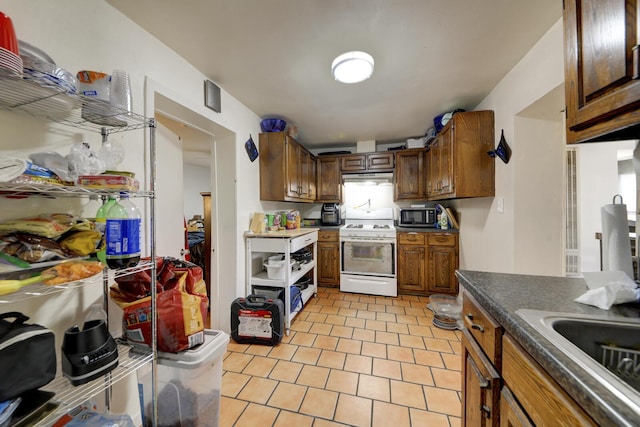 kitchen featuring light tile patterned floors, white range with gas cooktop, dark countertops, brown cabinets, and a sink