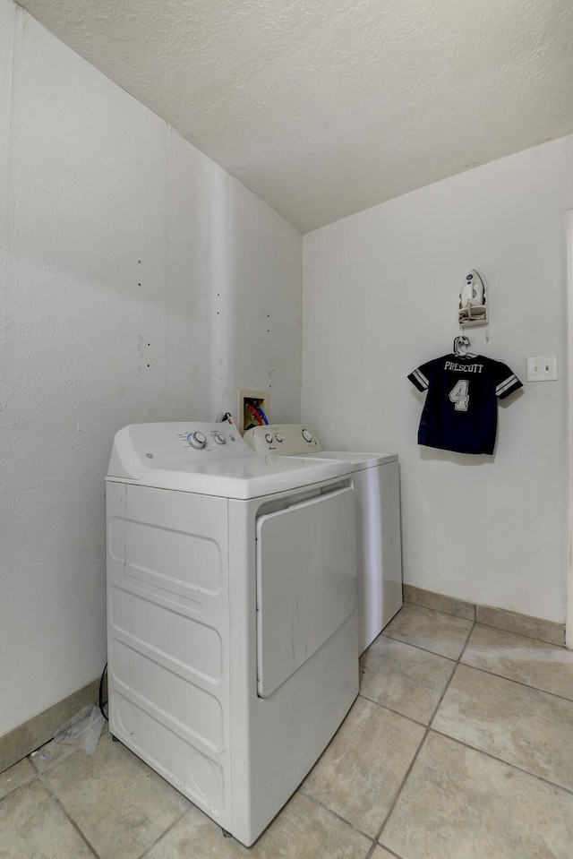 washroom with a textured ceiling, laundry area, washing machine and dryer, and baseboards