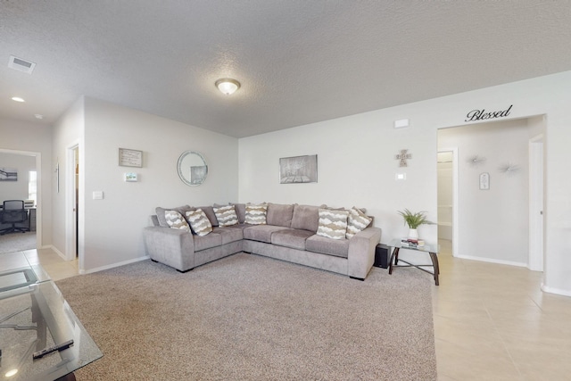 living area with a textured ceiling, light tile patterned floors, visible vents, and baseboards