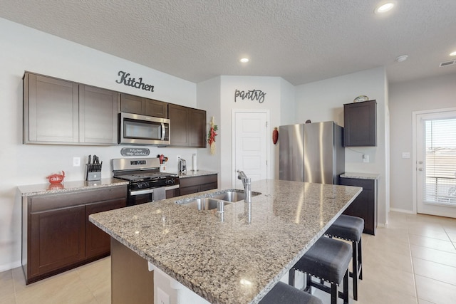 kitchen featuring a kitchen bar, light stone counters, stainless steel appliances, and a sink