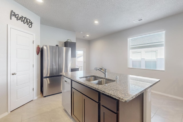 kitchen featuring visible vents, appliances with stainless steel finishes, a kitchen island with sink, a sink, and light stone countertops