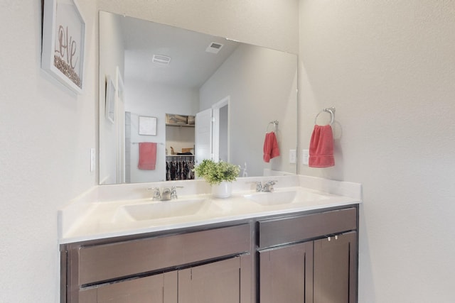 full bathroom with double vanity, a spacious closet, a sink, and visible vents