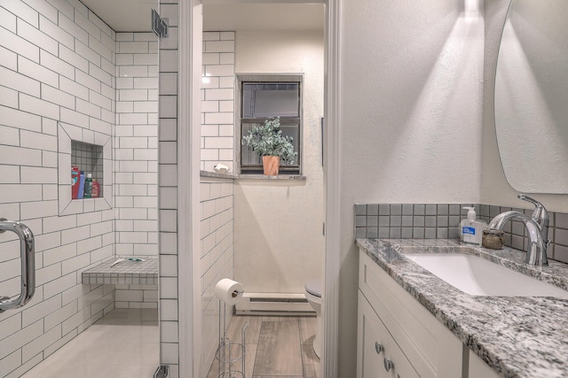 bathroom with a textured wall, toilet, baseboard heating, a shower stall, and vanity