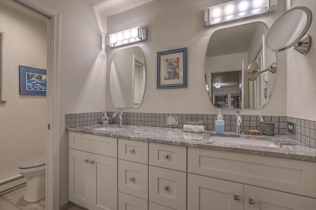 full bathroom with a baseboard radiator, a sink, toilet, and double vanity