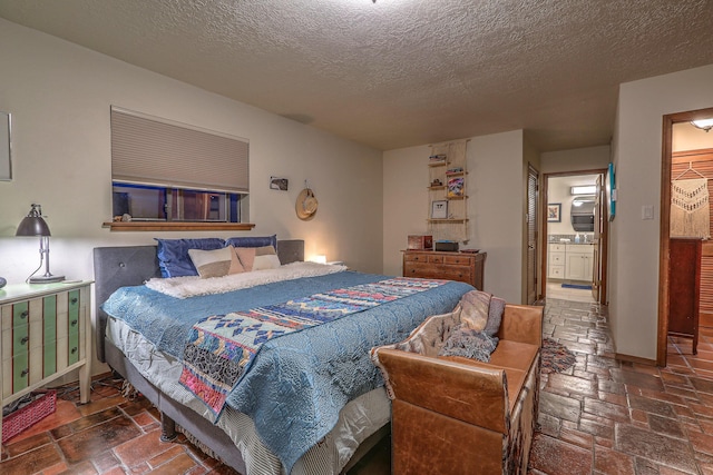 bedroom featuring a textured ceiling, stone tile floors, ensuite bath, and baseboards