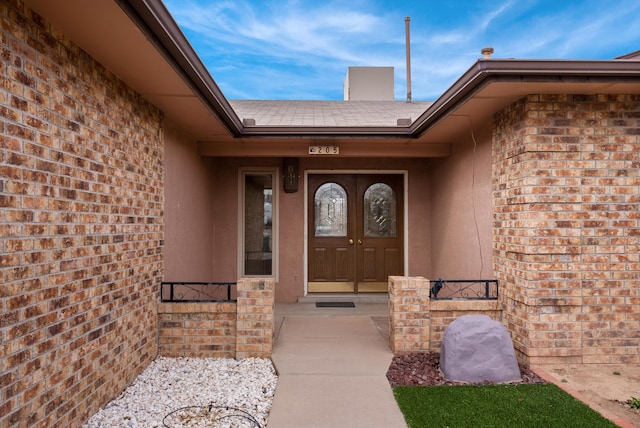 entrance to property featuring french doors, brick siding, and roof with shingles