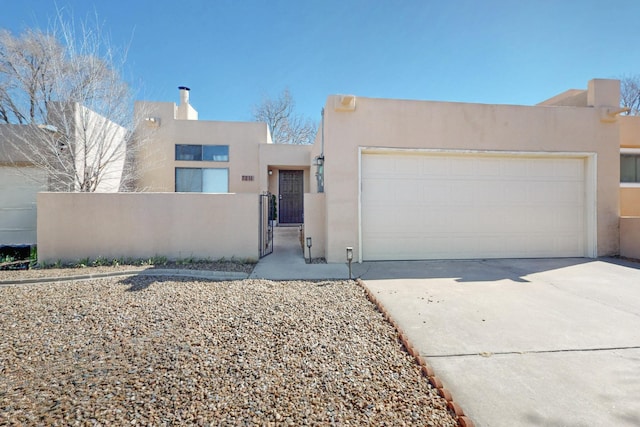 adobe home with an attached garage, fence, concrete driveway, a gate, and stucco siding