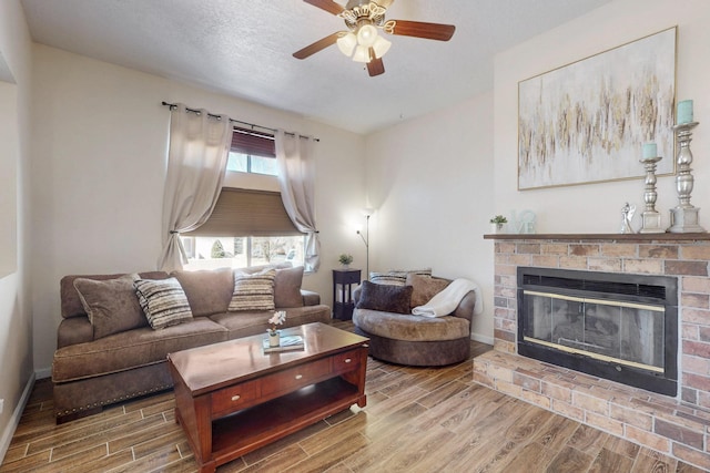 living area featuring a ceiling fan, wood tiled floor, a brick fireplace, and baseboards