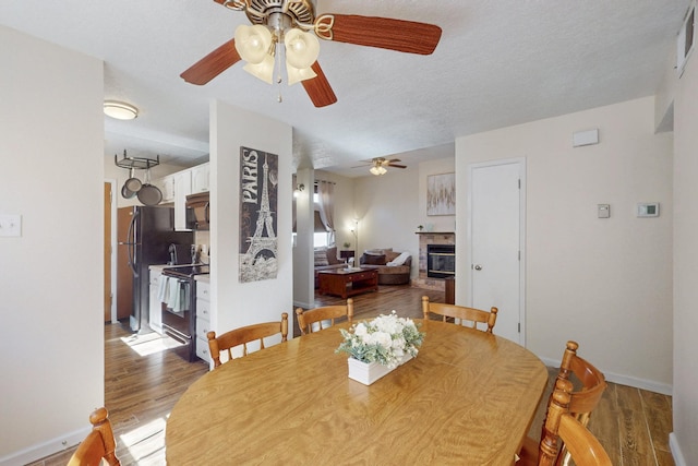 dining space with a textured ceiling, ceiling fan, a tile fireplace, light wood-style flooring, and baseboards