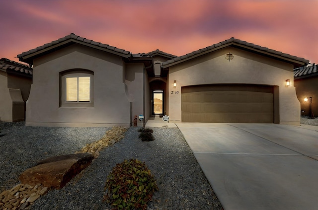 mediterranean / spanish-style home featuring stucco siding, a garage, driveway, and a tiled roof