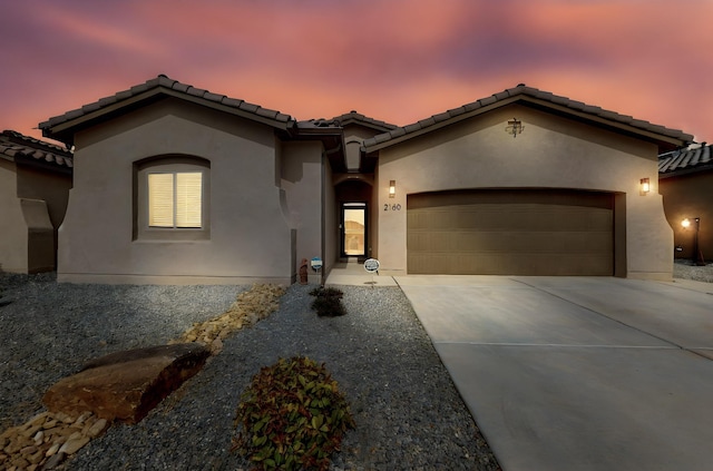 mediterranean / spanish-style house with a tile roof, an attached garage, driveway, and stucco siding
