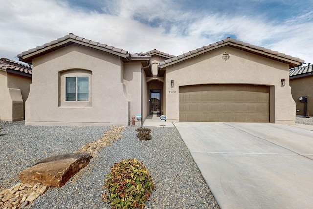 mediterranean / spanish house featuring stucco siding, driveway, a tile roof, and a garage