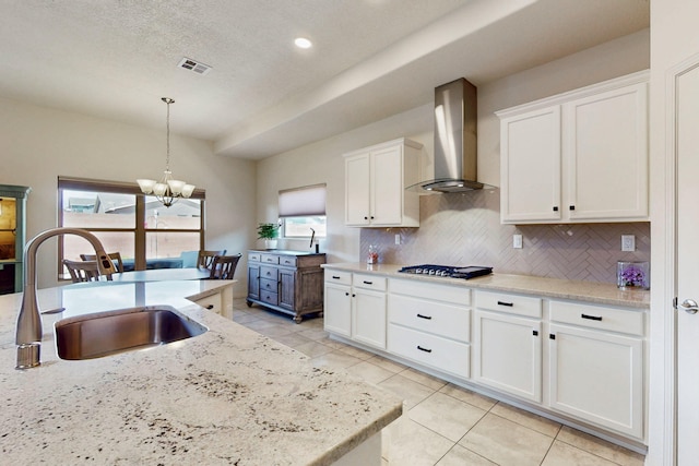 kitchen with a sink, a chandelier, wall chimney exhaust hood, white cabinetry, and visible vents