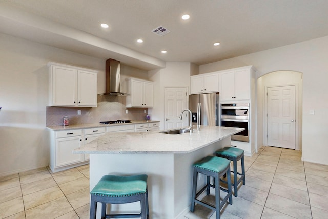 kitchen with a kitchen breakfast bar, stainless steel appliances, visible vents, wall chimney range hood, and a sink
