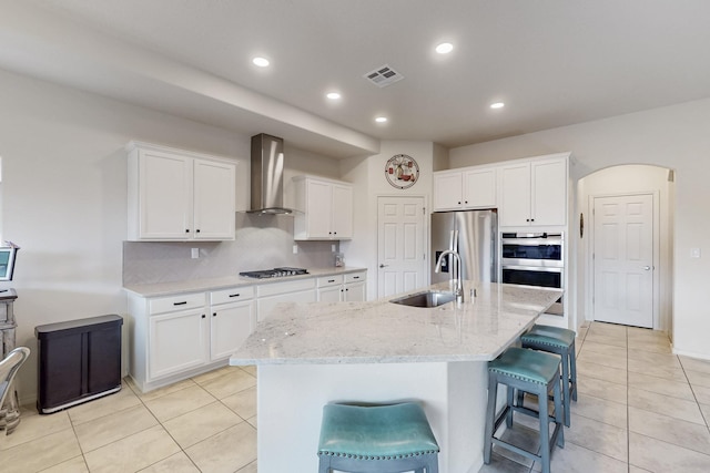 kitchen featuring visible vents, a sink, arched walkways, appliances with stainless steel finishes, and wall chimney exhaust hood