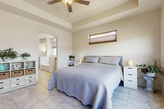 bedroom featuring arched walkways, light tile patterned floors, a ceiling fan, ensuite bath, and a raised ceiling