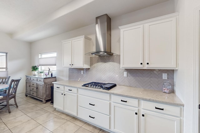 kitchen featuring light stone counters, stainless steel gas stovetop, white cabinets, wall chimney exhaust hood, and backsplash