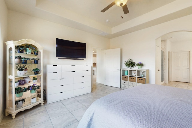 bedroom with a ceiling fan, arched walkways, a raised ceiling, and light tile patterned floors