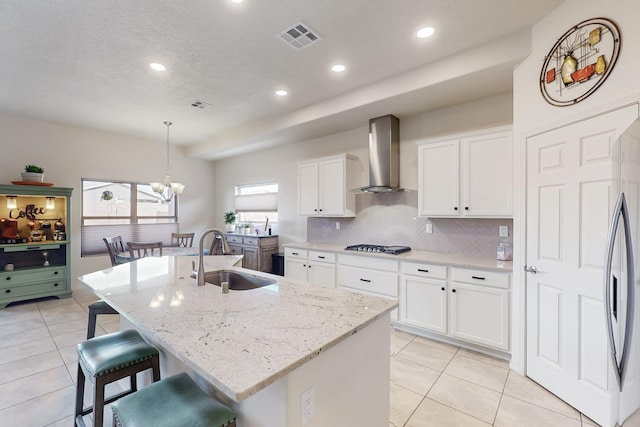 kitchen with light tile patterned floors, visible vents, a kitchen island with sink, a sink, and wall chimney range hood