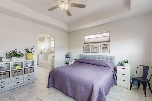 bedroom with a raised ceiling, light tile patterned floors, and arched walkways