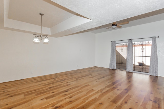 spare room with ceiling fan with notable chandelier, a tray ceiling, a textured ceiling, and wood finished floors