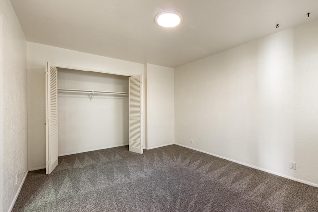 unfurnished bedroom featuring baseboards, dark colored carpet, and a closet