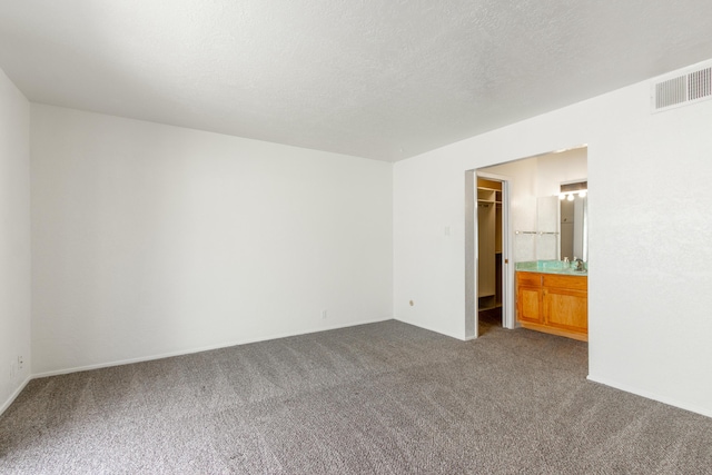 unfurnished bedroom with dark colored carpet, a walk in closet, visible vents, and a textured ceiling