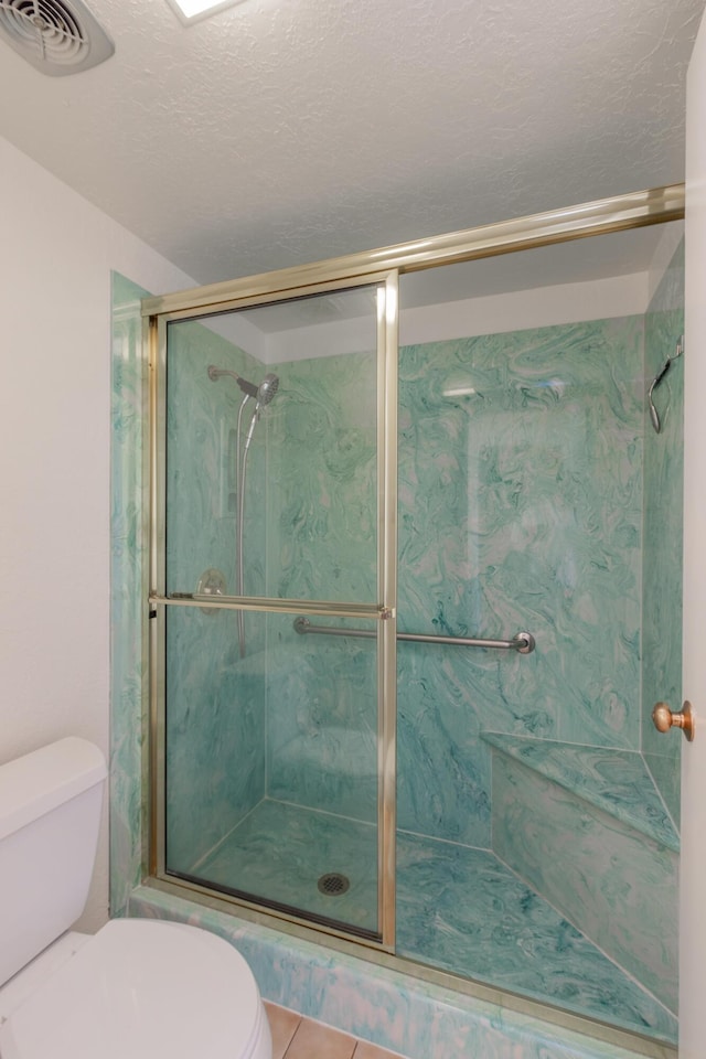 bathroom featuring a stall shower, visible vents, a textured ceiling, and toilet