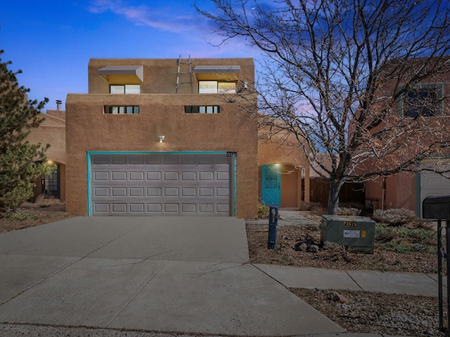 pueblo-style home with concrete driveway, an attached garage, and stucco siding