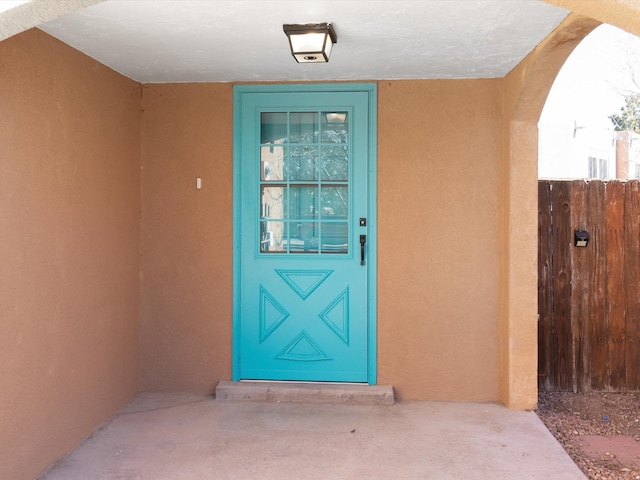 view of exterior entry featuring fence and stucco siding