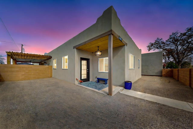 back of property at dusk featuring a patio, a pergola, fence, and stucco siding