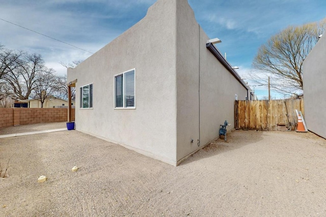 view of side of property featuring fence, a patio, and stucco siding