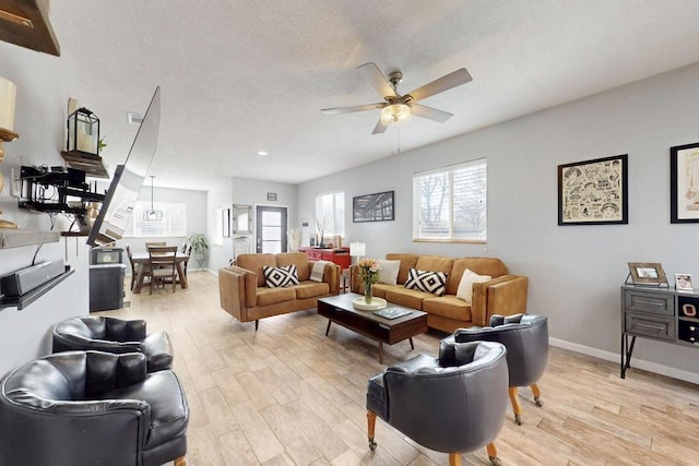 living room with a ceiling fan, light wood-type flooring, a textured ceiling, and baseboards