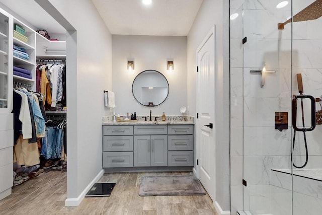 full bathroom with a stall shower, a spacious closet, vanity, and wood finished floors