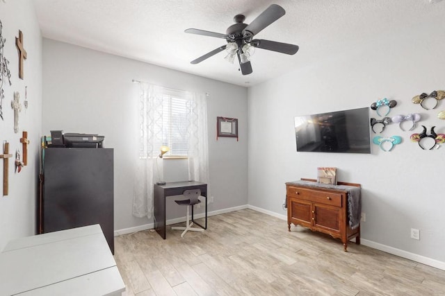 interior space featuring light wood finished floors, ceiling fan, baseboards, and a textured ceiling