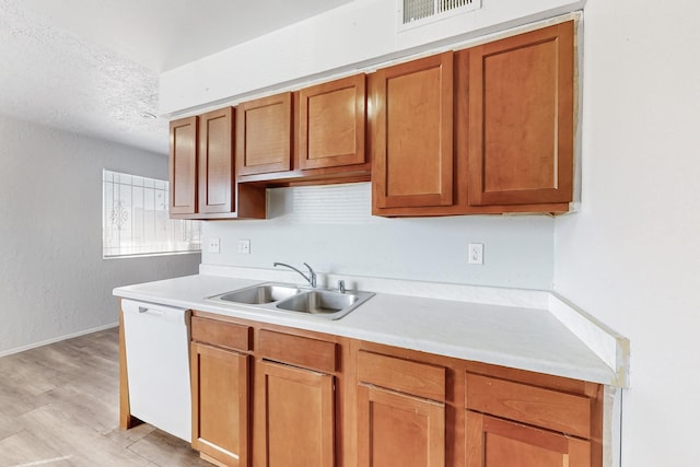 kitchen with visible vents, brown cabinetry, dishwasher, light countertops, and a sink