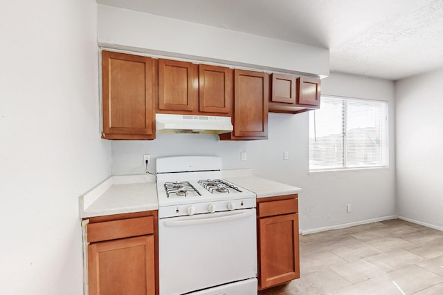 kitchen with brown cabinetry, light countertops, under cabinet range hood, and white gas range