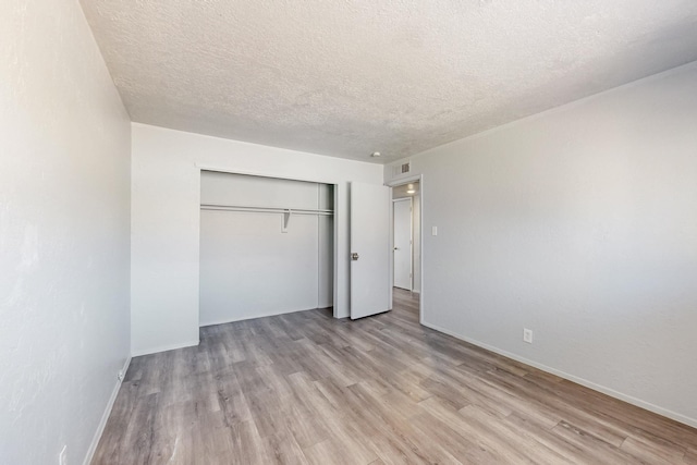 unfurnished bedroom featuring visible vents, baseboards, a textured ceiling, light wood-style floors, and a closet