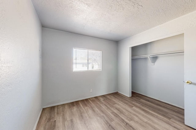 unfurnished bedroom with a textured ceiling, a textured wall, wood finished floors, baseboards, and a closet