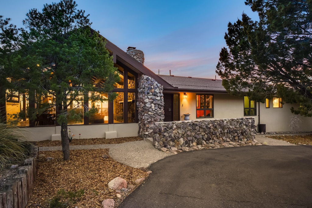 mid-century inspired home with stone siding, a chimney, a sunroom, and stucco siding