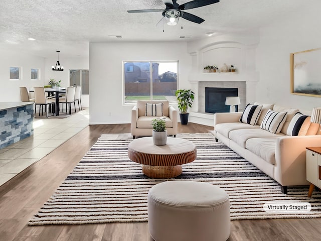 living room with a textured ceiling, a fireplace, wood finished floors, and a ceiling fan