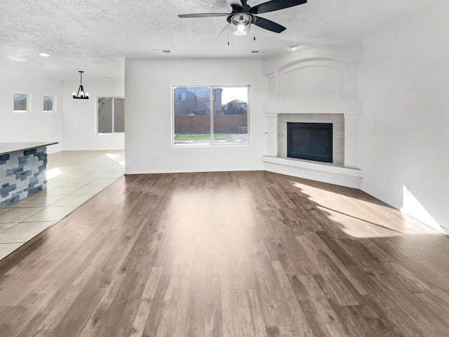 unfurnished living room with a fireplace, ceiling fan with notable chandelier, a textured ceiling, and wood finished floors