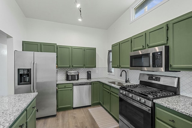 kitchen with stainless steel appliances, backsplash, light wood-style floors, a sink, and green cabinetry