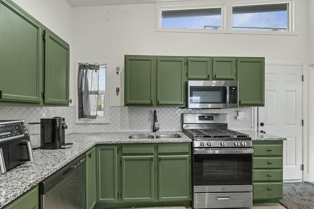 kitchen featuring stainless steel appliances, a sink, green cabinets, and light stone countertops