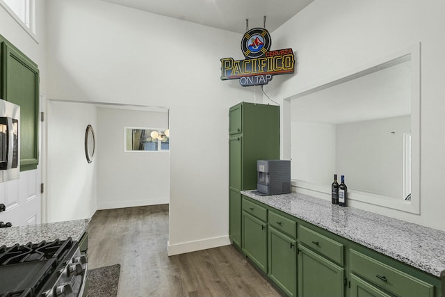 kitchen featuring baseboards, dark wood-style flooring, light stone countertops, stainless steel range with gas cooktop, and green cabinets