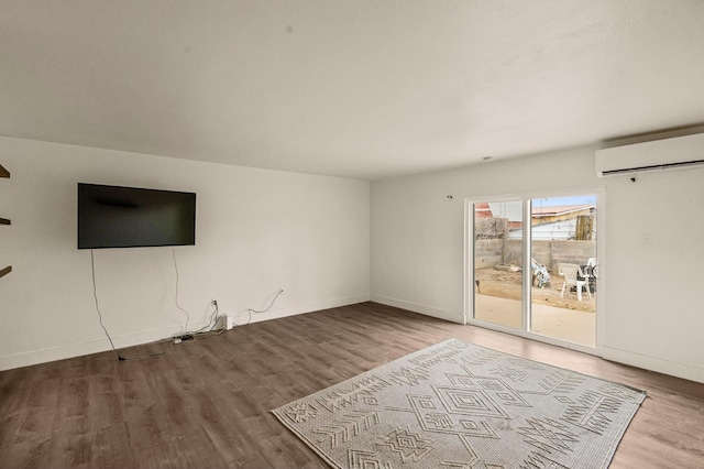 unfurnished living room featuring an AC wall unit, wood finished floors, and baseboards