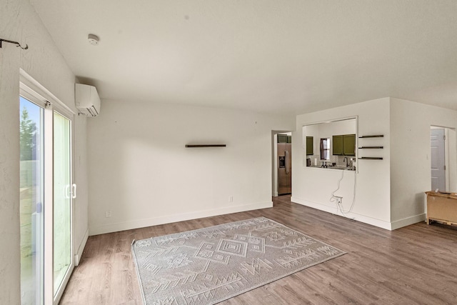 unfurnished living room with a wall unit AC, baseboards, and wood finished floors