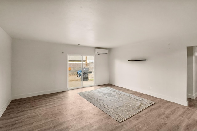 spare room with an AC wall unit, baseboards, and wood finished floors