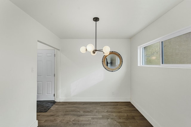 unfurnished dining area featuring baseboards, wood finished floors, and an inviting chandelier