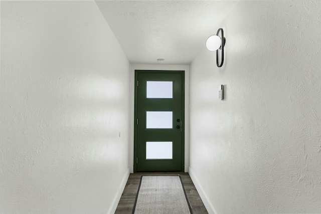 doorway with a textured wall, dark wood finished floors, a textured ceiling, and baseboards